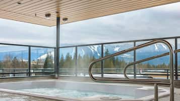 A hot tub with a view of snow-capped mountains, a wooden ceiling, and a metal railing.