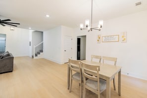 Ein Essbereich mit Tisch und Stühlen, Deckenventilator, Einbauleuchten und einer Treppe zu einem weiteren Raum.