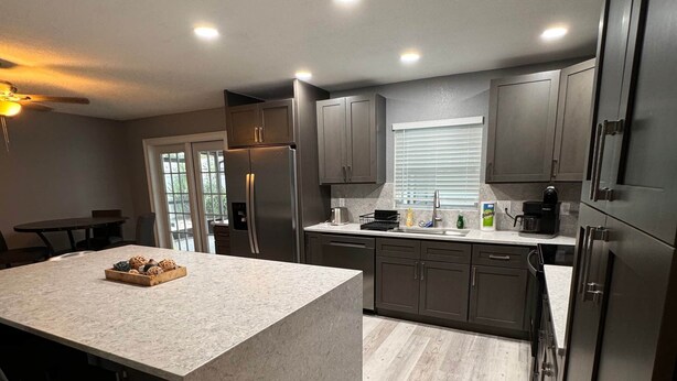A modern kitchen with a large island, dark cabinets, and a window with blinds. - Pet Friendly Pool Home close to IRB and Walsingham Park (Seminole)