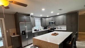 A modern kitchen with a central island, stainless steel appliances, and a ceiling fan. - Pet Friendly Pool Home close to IRB and Walsingham Park (Seminole)