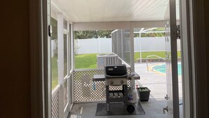 En uteplats med en grill, en gasolflaska och en pool i bakgrunden.