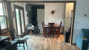 Een ruime woonkamer met een houten vloer, een eettafel met stoelen, een open haard en een blauwe bank.