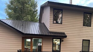 Een tweelaags huis met een terras, schoorsteen en een groot raam.