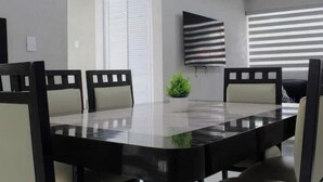 Une salle de conférence avec une table en verre, des chaises noires, une plante en pot et un téléviseur fixé au mur.