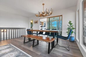 Ein Essbereich mit einem Holztisch, Bänken und Stühlen, einer Chandelüster und einem großen Spiegel.