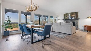 Una sala moderna con chimenea, ventanas amplias y un comedor con sillas azules.