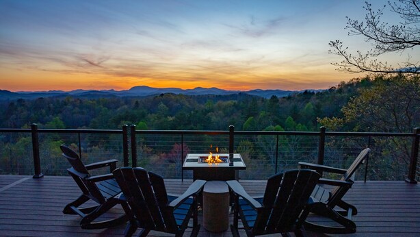 Una terraza con dos sillas Adirondack y un hoyo para el fuego, con vistas a una cordillera boscosa.