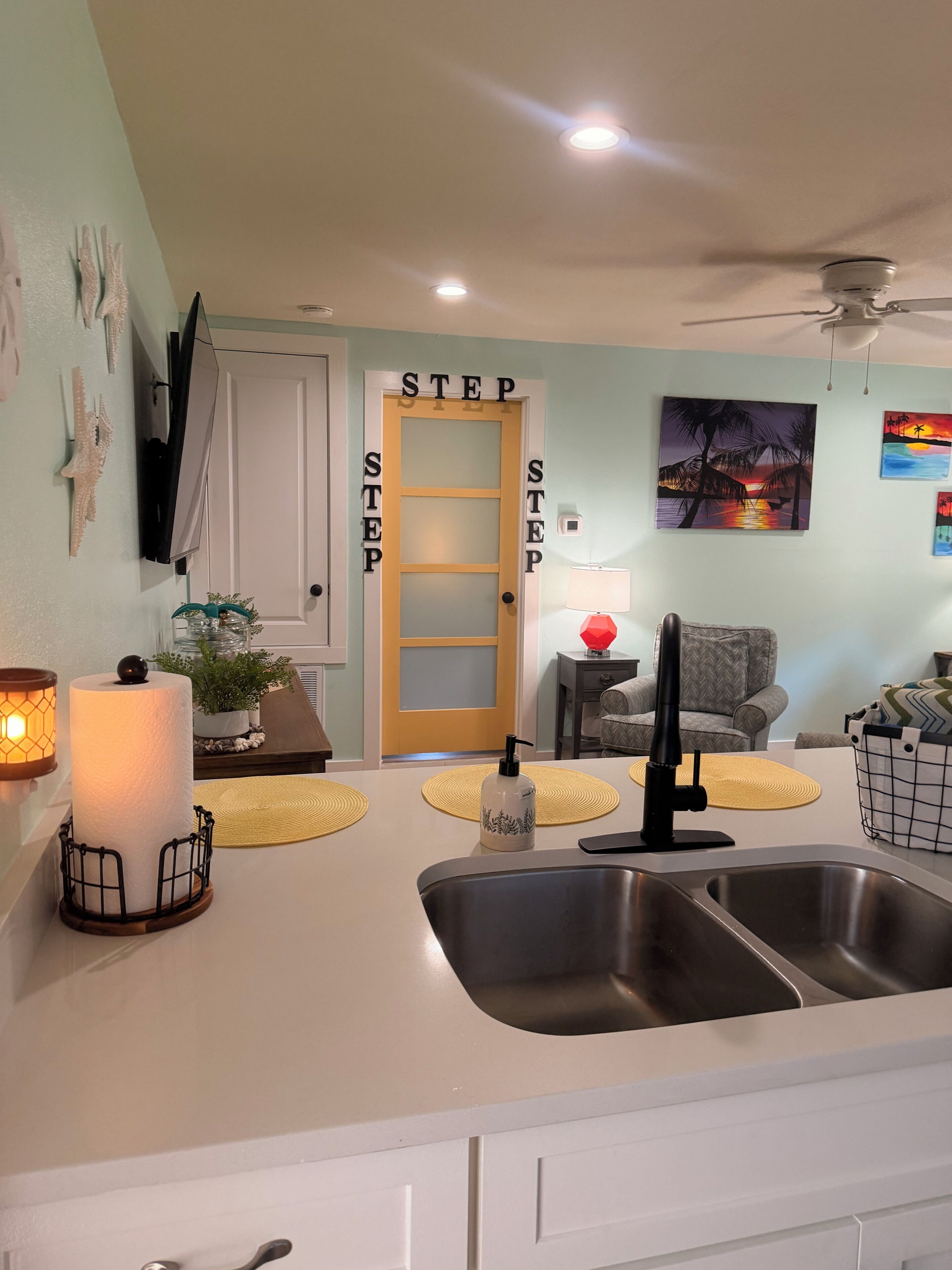 A kitchen with a sink, a countertop with a soap dispenser, and a door with 'STEP' signs.