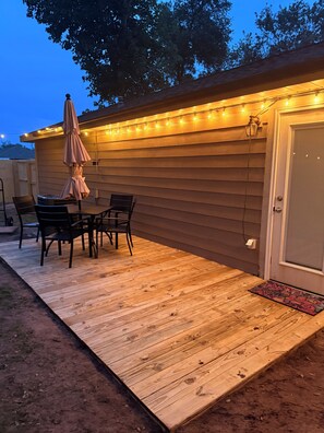 Eine Holzterrasse mit Tisch und Stühlen, einem überdachten Sonnenschirm und Lichterketten.