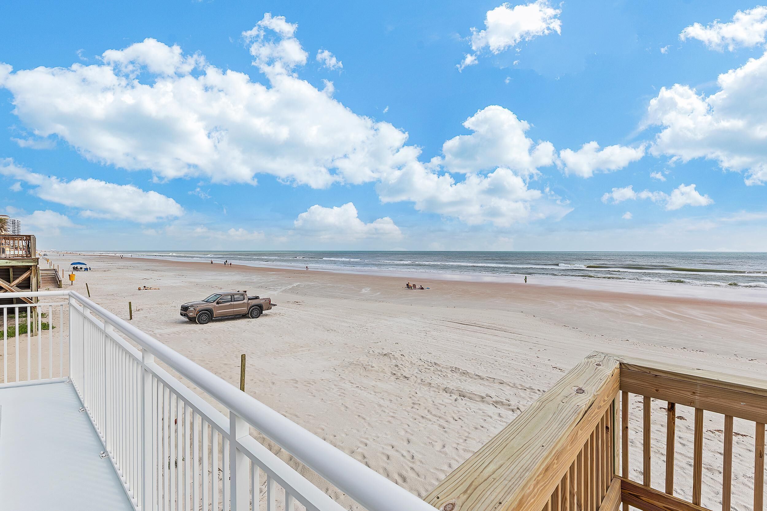 A beach view from a balcony with a wooden deck, sandy beach, and ocean.