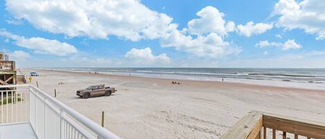 A beach view from a balcony with a wooden deck, sandy beach, and ocean.