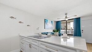 A modern kitchen with white cabinetry, a central island, and a view of the city through large windows. - Ocean Breeze Resort 213 (Daytona Beach Shores)