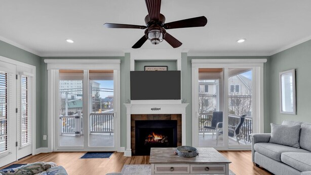 A living room with a fireplace, a ceiling fan, and a view through large sliding glass doors. - 10th Street Beach Block Condo (Ocean City)