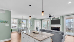 A modern kitchen with a central island, dining area, and a living room with a fireplace. - 10th Street Beach Block Condo (Ocean City)