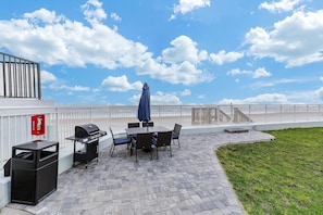 An outdoor patio with a grill, table, chairs, and a trash bin. - Ocean Breeze Resort 106 (Daytona Beach Shores)