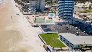 A coastal hotel with a beach view, a tennis court, and a parking lot. - Ocean Breeze Resort 106 (Daytona Beach Shores)