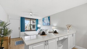 A modern kitchen with white cabinetry, a central island, and a view of a balcony. - Ocean Breeze Resort 106 (Daytona Beach Shores)