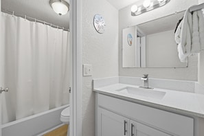 A bathroom with a shower curtain, a sink, a mirror, and a towel rack. - Ocean Breeze Resort 106 (Daytona Beach Shores)