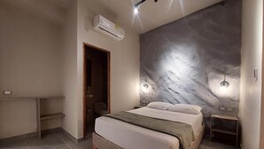 Un dormitorio con cama, aire acondicionado en la pared, una puerta y una mesita de noche con lámpara.