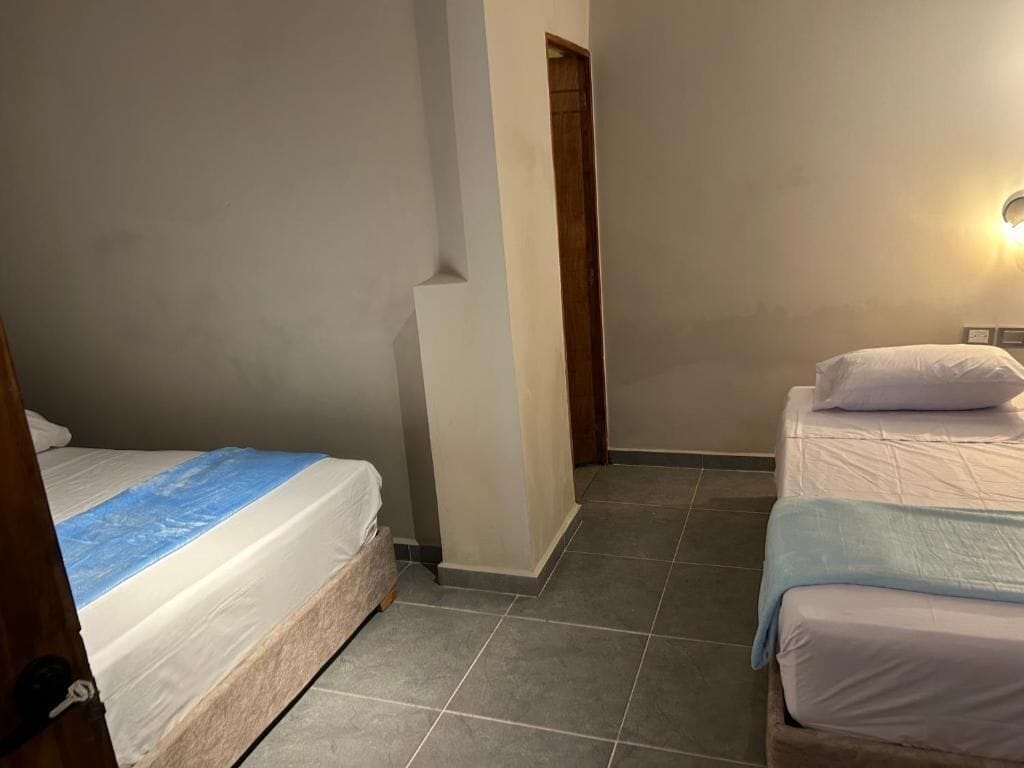 Una stanza con due letti, una porta e un punto luce a parete.