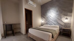 Un dormitorio con cama, aire acondicionado de pared, una puerta y una mesita pequeña.
