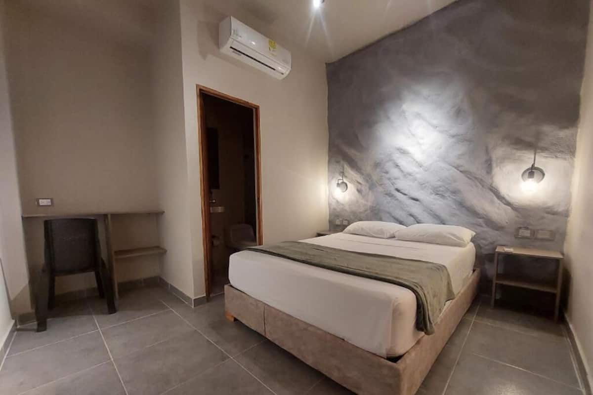 Un dormitorio con cama, aire acondicionado de pared, una puerta y una mesita pequeña.