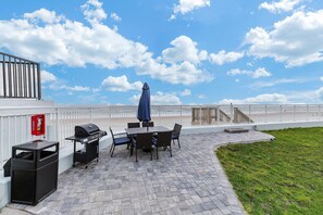 An outdoor patio with a grill, table, chairs, and a trash bin. - Ocean Breeze Resort 109 (Daytona Beach Shores)