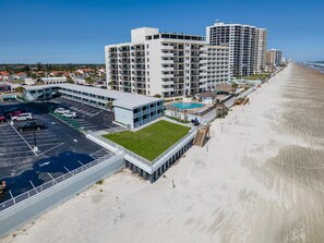 A beachfront hotel with multiple high-rise buildings, a parking lot, and a swimming pool. - Ocean Breeze Resort 109 (Daytona Beach Shores)
