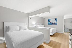A modern hotel room with a large bed, a smaller bed, a desk, and a painting on the wall. - Ocean Breeze Resort 109 (Daytona Beach Shores)