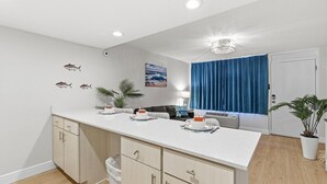 Una cucina moderna con un piano di lavoro bianco, mobili in legno e una tenda blu.