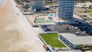 Un hotel sulla costa con vista sulla spiaggia, un campo da tennis e un parcheggio.