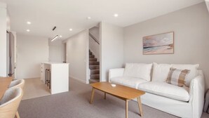 A modern living room with a white sofa, a wooden coffee table, and a painting on the wall.