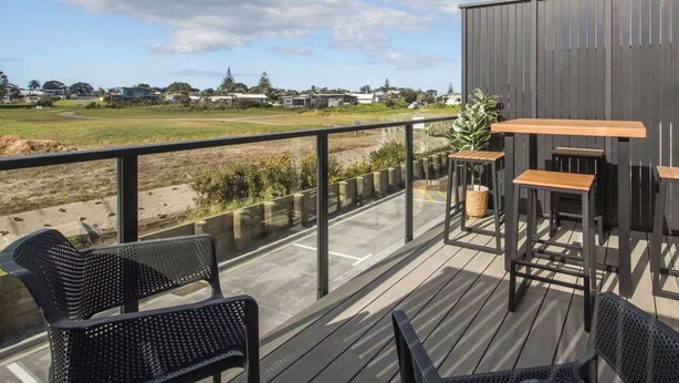 A deck with outdoor seating, a view of a field, and a building in the background.