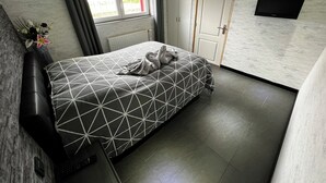 Een moderne slaapkamer met een bedovertrek met een geometrisch patroon, een flatscreen-tv aan de wand, een radiator en een raam met gordijnen.