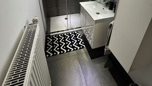 Een moderne badkamer met een douchecabine van glas, een wit wastafeltje en een spiegel.