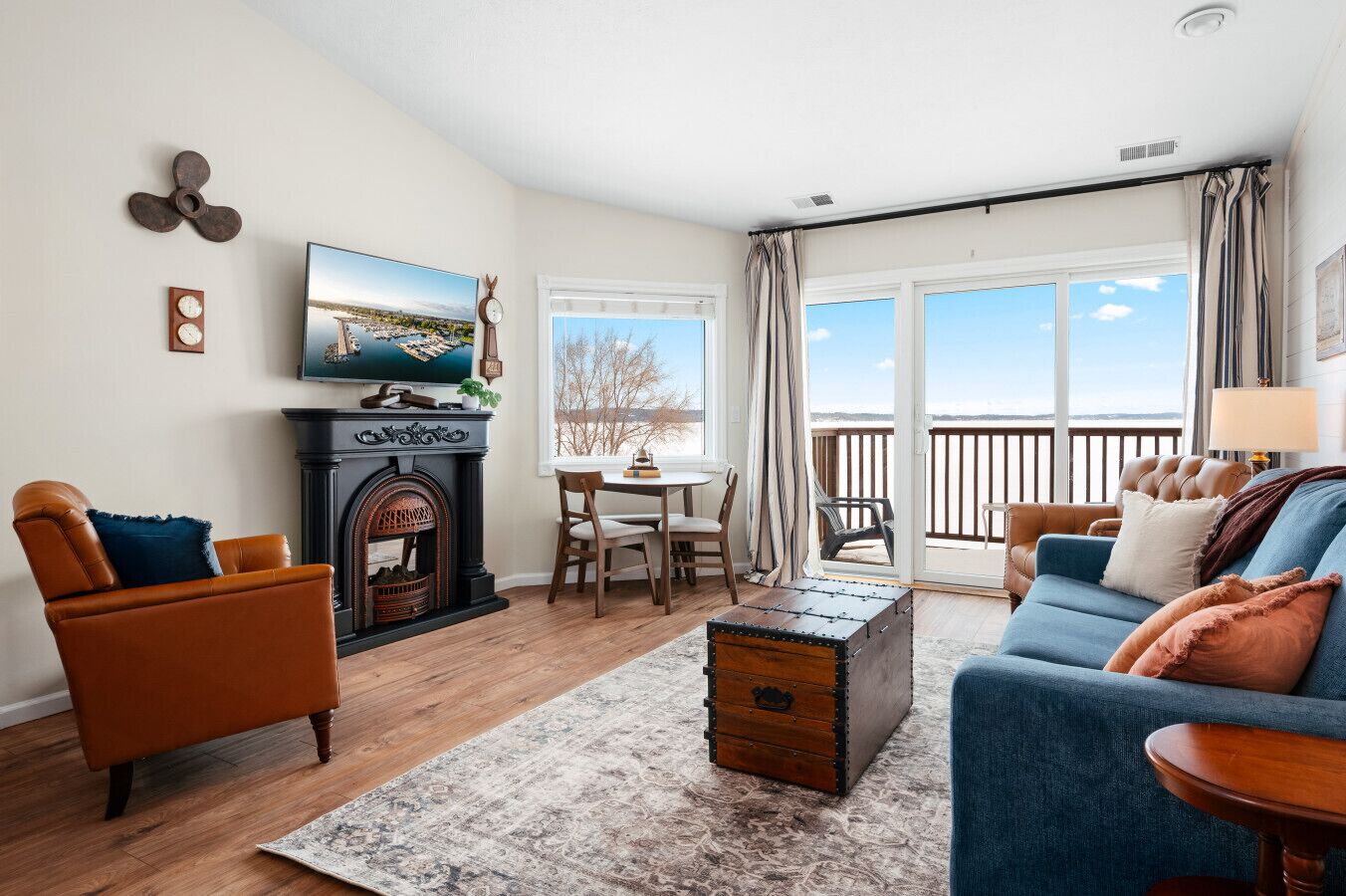 Ein Wohnzimmer mit Kamin, Fernseher, Esstisch mit Stühlen, einer Couch und Blick ins Freie.