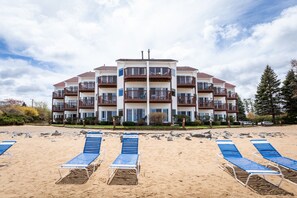 A beachfront hotel with multiple balconies, a sandy beach in front, and blue lounge chairs. - Stateroom 322|Beachfront Condo|Downtown + Tart Trail (Traverse City)