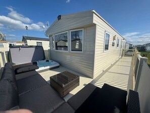 A mobile home with a patio area, including a hot tub, outdoor seating, and a small table. - Fantasy Island Resort - The Merlin with Private Hot Tub - Eastgate D7 (Ingoldmells)