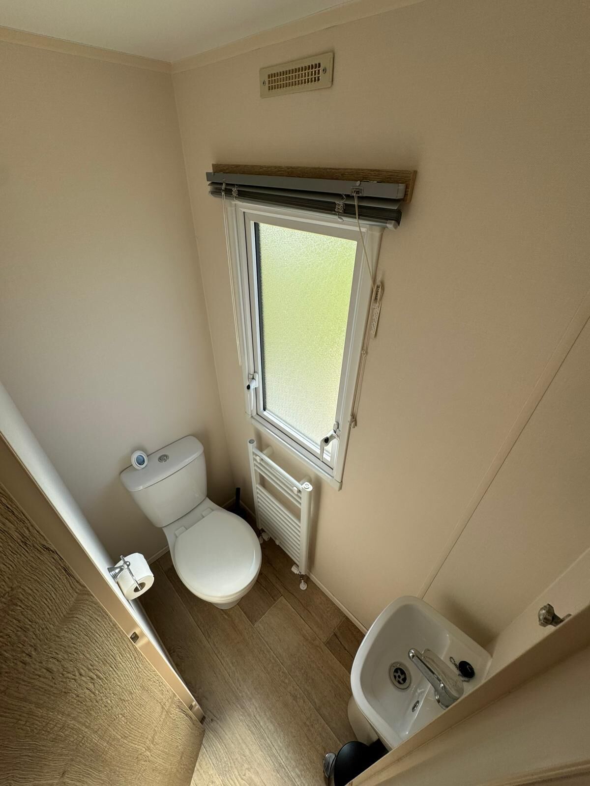Un baño pequeño con inodoro, ventana, radiador y lavamanos.
