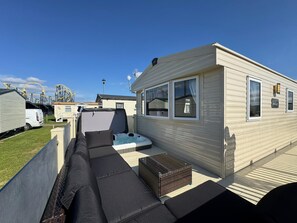 Ein Mobilheim mit einer Terrasse, inklusive einer Sitzecke, einem Whirlpool und einem kleinen Tisch.