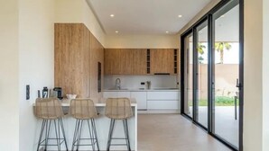 A modern kitchen with wooden cabinets, a white countertop, and three bar stools. - Sumptuous Villa with swimming pool in the secure estate of MYSK Route d'amizmiz (Marrakech)