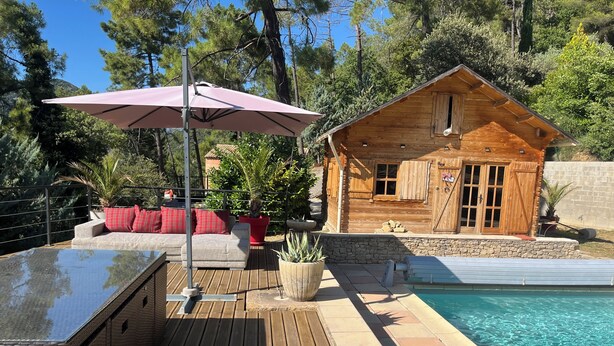 Una cabaña de madera con piscina, una terraza amueblada al aire libre y un muro de piedra.
