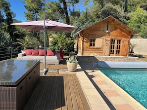 A wooden cabin with a pool, a deck with outdoor furniture, and a stone wall.