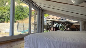 Un dormitorio con un gran ventanal, piso de madera y una cama con ropa de cama blanca.