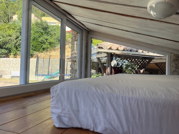 A bedroom with a large window, wooden floor, and a bed with white bedding.