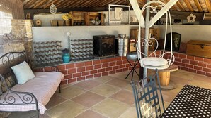 Un interior rústico con pared de ladrillo, techo de madera, una silla colgante, un banco y suelo de baldosas.