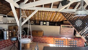Un espacio de descanso rústico al aire libre con pared de ladrillo, una silla colgante, una mesa y un dardo.