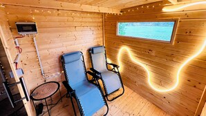 En stuga med träpanel, inredd med två fåtöljer, ett litet bord, ett fönster med utsikt och ljusslingor.
