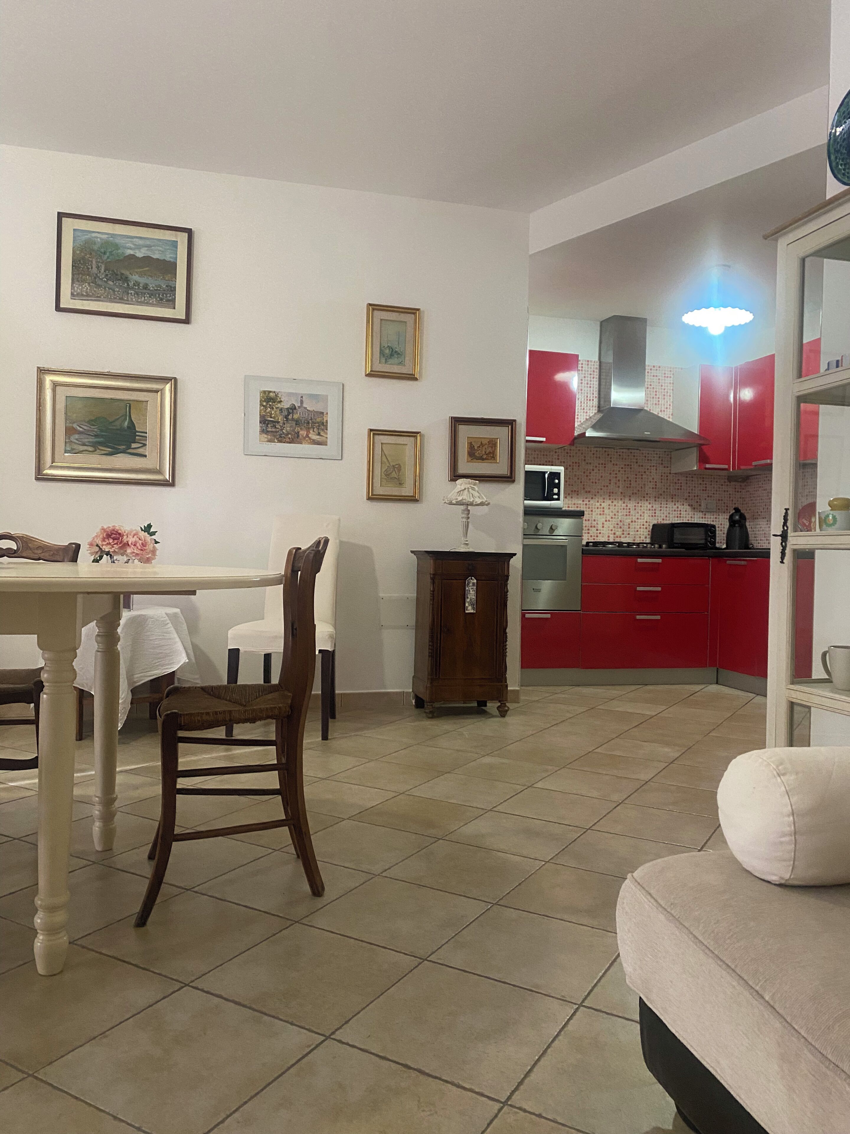 A dining area with a table and chairs, a kitchen with red cabinets, and a tiled floor.