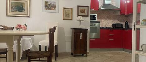 A dining area with a table and chairs, a kitchen with red cabinets, and a tiled floor.